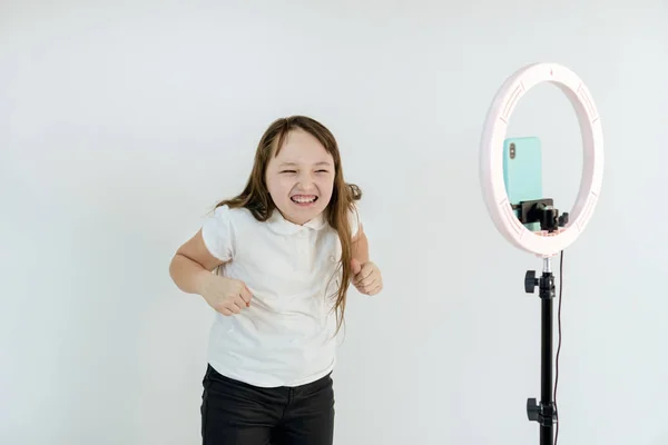 Ein Teenager-Mädchen tanzt und dreht ein Video. Selfies. Das Telefon ist auf einem Stativ montiert und die Ringlampe leuchtet — Stockfoto