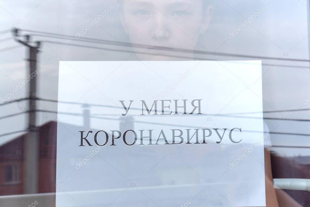 The girl is holding a sign with an inscription in Russian. I have a coronavirus. Photo taken through glass.