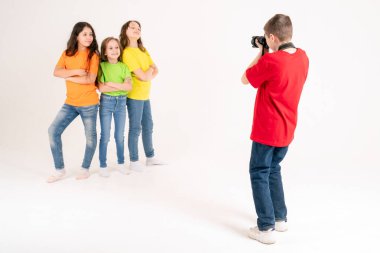 Bir erkek fotoğrafçı stüdyoda beyaz bir arka planda parlak tişörtlü üç tatlı kızın fotoğraflarını çekiyor. Genç fotoğrafçı ve blog yazarı.