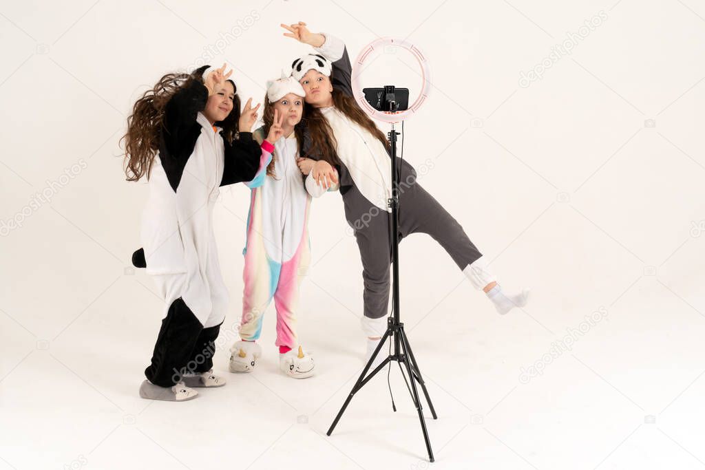 Cute teenage girls in kigurumi and sleep masks smiling and shoots a video. Selfies. The phone is mounted on a tripod and the ring lamp shines.