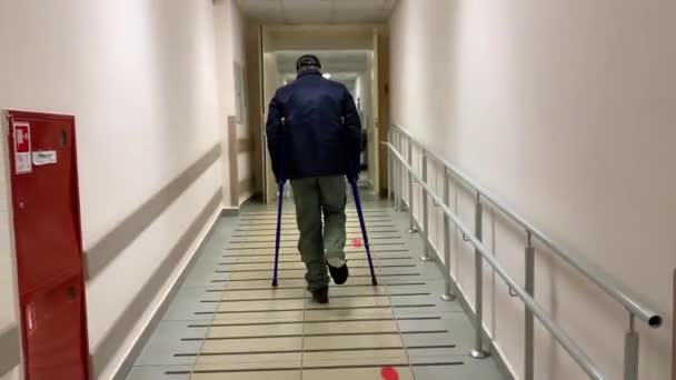 Een man in een gips die op krukken loopt langs de ziekenhuisgang. Rusland, Tatarstan, 05 april 2020. — Stockvideo