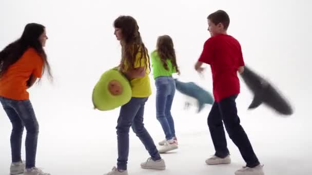 子供保護の日 10代の子供たちのグループは 彼らの手の中に柔らかいおもちゃを保持し お互いと遊んでいます スタジオ撮影 枕の戦いの概念 3人の少女と1人の少年 — ストック動画