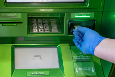 Bir ATM 'nin arka planında tıbbi koruyucu eldivenin içinde kredi kartıyla. Rusya, Tataristan, 18 Nisan 2020.