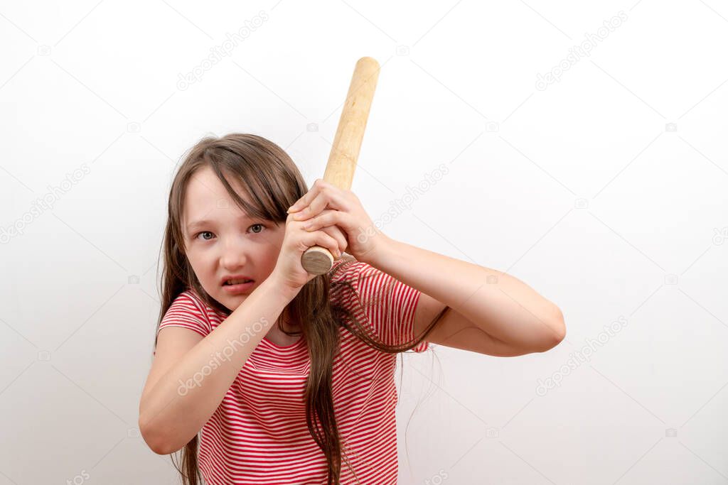 Girl teenager with a rolling pin in her hands aggressively looks at the camera on a white background. The concept of emotions and domestic violence