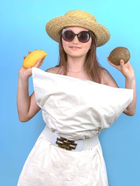 Mavi arka planda, elbise yerine beyaz yastık ve şık bir şapka takan bir kız. Genç kız karantinada eğleniyor ve moda defilesi düzenliyor.