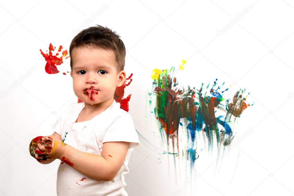 3 year old boy stained with paint on the background of a painted wall. Colored hands. The concept of early development of children. School of childrens drawing