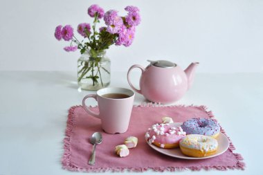 Pembe çaydanlık, bir fincan çay ve renkli lezzetli çörekler.