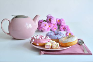 Pembe çaydanlık, bir fincan çay ve renkli lezzetli çörekler.