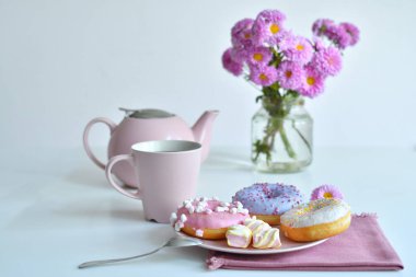 Pembe çaydanlık, bir fincan çay ve renkli lezzetli çörekler.