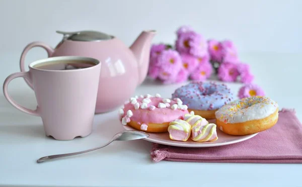 Розовый чайник, чашка чая и красочные вкусные пончики — стоковое фото