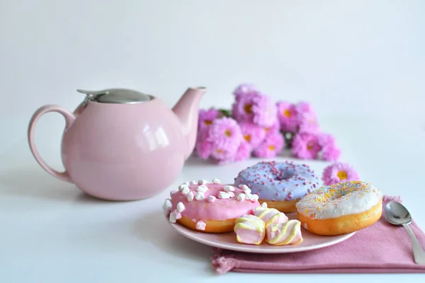 Розовый чайник, чашка чая и красочные вкусные пончики — стоковое фото