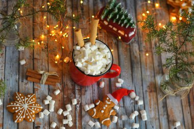 Kakao ya da kırsal masada lokum kaplı sıcak çikolata. Noel veya Yeni Yıl kompozisyonu. Baston şekerli zencefilli adam. Kırmızı bardakta maytaplı şekerlemenin yakın görüntüsü. yumuşak seçici odak.