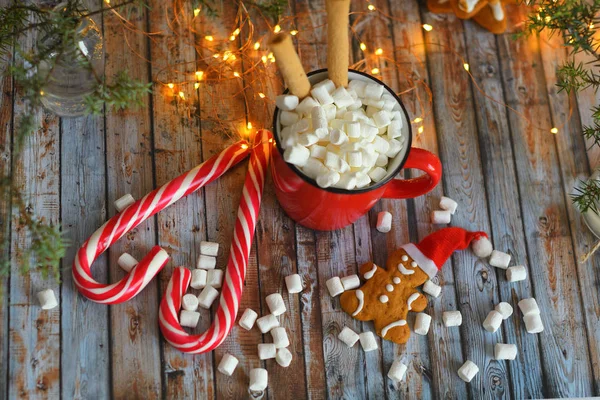 Cacao o chocolate caliente con malvavisco sobre mesa rústica. Composición de Navidad o Año Nuevo. Hombre de jengibre con bastón de caramelo. Vista cercana de malvavisco en taza roja con espumoso. enfoque selectivo suave . — Foto de Stock