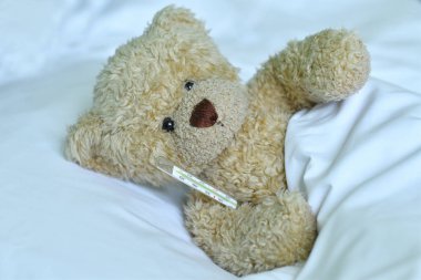 Beyaz arka planda cıva termometresi olan oyuncak ayı.