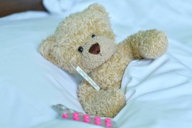 Beyaz arka planda cıva termometresi olan oyuncak ayı.