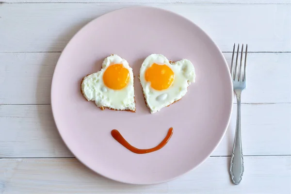 Two fried eggs on pink plate for healthy breakfast on wooden table. top view