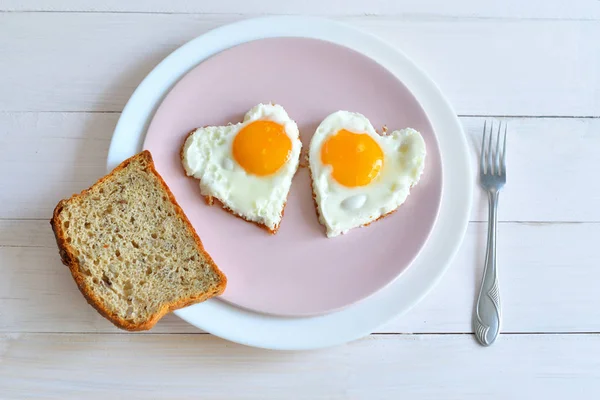 木製のテーブルの上で健康的な朝食のためのピンクのプレート上の2つの揚げ卵。トップビュー — ストック写真