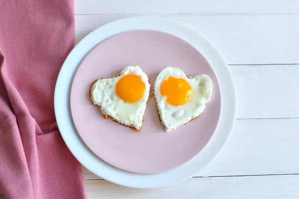 Two fried eggs on pink plate for healthy breakfast on wooden table. top view