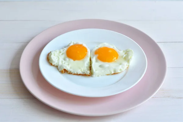 Two fried eggs on pink plate for healthy breakfast on wooden table. top view