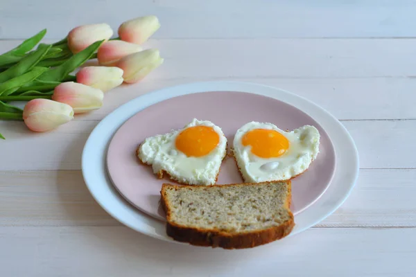 Petit déjeuner le jour de la Saint-Valentin - œufs frits en forme de coeur et bouquet de tulipes roses. — Photo