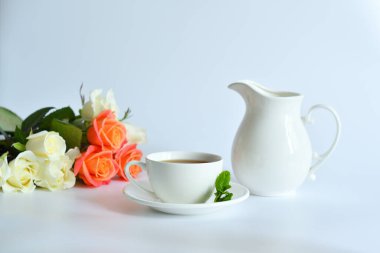 Beyaz arka planda bir buket gülün yanında nane ve sürahi ile küçük bir fincan çay. Sağlıklı bir hayat. Şekersiz. Seçici odaklanma. Boşluğu kopyala