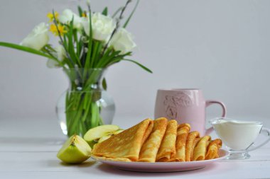 Pancake week: thin pancakes with berries and glass of milk on white table.french crepes .Glass vaza with a bouquet of spring flowers.Delicious breakfast.Selective focus