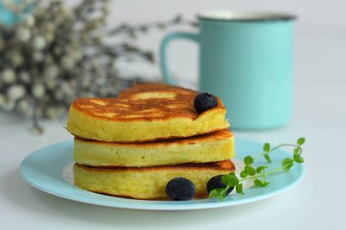 Sağlıklı kahvaltı için mavi tabakta Amerikan gözlemeleri bahar çiçekleriyle beyaz masada. Sevgililer Günü veya 8 Mart 'ta kahvaltı. Kalp şeklinde krepler.