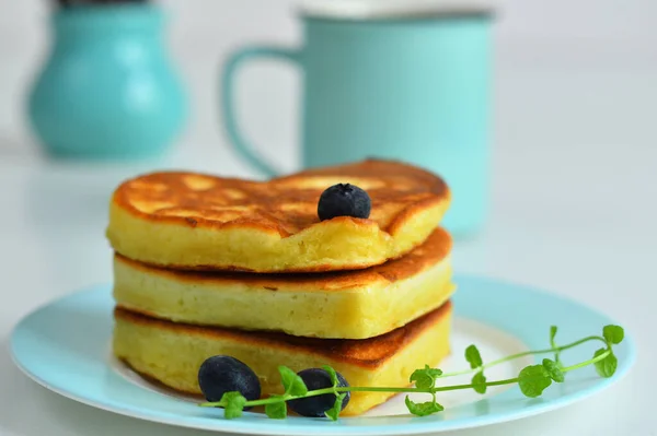 American pancakes on blue plate for healthy breakfast on white table with spring flowers.Breakfast on Valentine\'s Day or 8 March - pancakes in the shape of a heart.Pancake week.Selective focus