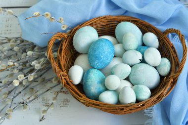 Hasır bir sepette mavi Paskalya yumurtaları ve arka planda söğüt çiçekleri. Doğal olarak mermer taşlı amber çiçeğiyle boyanmış yumurtalar. Eko boya. Mutlu Paskalya kartları. Seçmeli odaklanma..