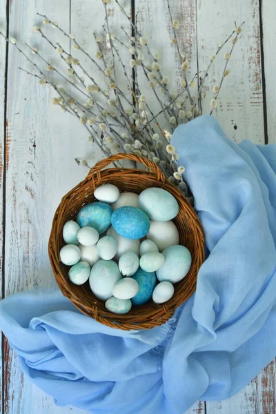 blue Easter eggs in a wicker basket and bouquet of willow flowers on light background.Naturally Eggs painted with hibiscus with marble stone effect. Eco paint. Happy Easter card.Selective focus.