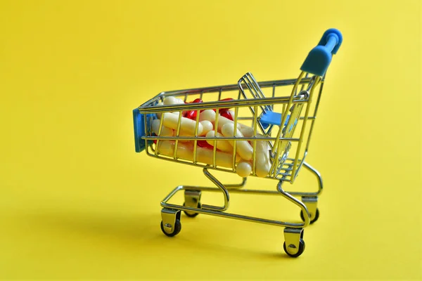 黄色の背景に各種薬の丸薬でショッピングカート ドラッグストア オンライン薬局 製薬会社のビジネスコンセプトのための創造的なアイデア — ストック写真