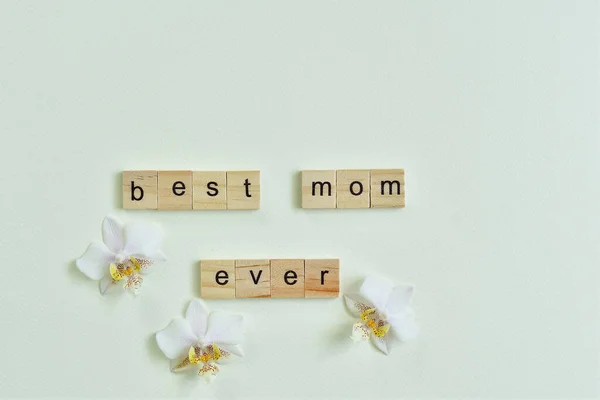 BEST MOM EVER text with delicate orchid flower on light background. Mother's day creative concept