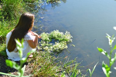 Beyaz elbiseli güzel kız nehir yüzeyine çiçek çelengi koyuyor. Ivan Kupala bayramı. Yaz dönümü. Dünya Günü. Ivan Kupala 'nın Pagan bayramı. Seçmeli odak noktası.