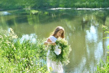 Nehir kenarındaki yaz çayırında güzel çelenkli bir kız. Ivan Kupala bayramı. 7 Temmuz, Ukrayna 'da falcılık ve kehanet ayinleriyle geleneksel Slav bayramı.