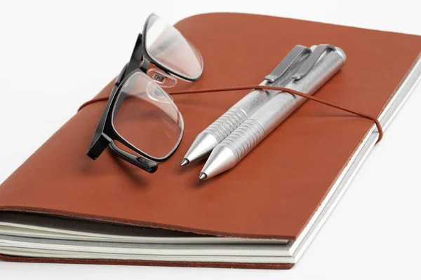 Couverture de journal en cuir rouge avec stylos et lunettes — Photo