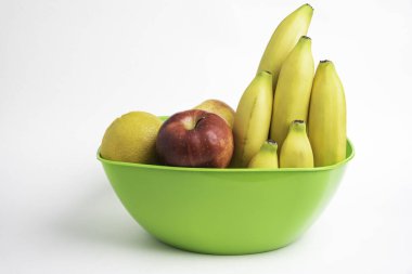 Elmalar, muzlar, portakallar ve diğerleri gibi sanatsal olarak düzenlenmiş taze ve olgun meyvelerle dolu parlak yeşil bir plastik kase..