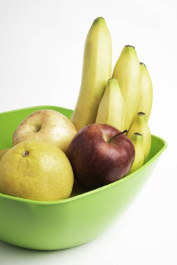 Elmalar, muzlar, portakallar ve diğerleri gibi sanatsal olarak düzenlenmiş taze ve olgun meyvelerle dolu parlak yeşil bir plastik kase..