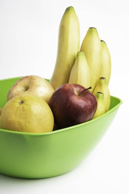 Elmalar, muzlar, portakallar ve diğerleri gibi sanatsal olarak düzenlenmiş taze ve olgun meyvelerle dolu parlak yeşil bir plastik kase..