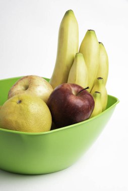 Elmalar, muzlar, portakallar ve diğerleri gibi sanatsal olarak düzenlenmiş taze ve olgun meyvelerle dolu parlak yeşil bir plastik kase..