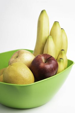 Elmalar, muzlar, portakallar ve diğerleri gibi sanatsal olarak düzenlenmiş taze ve olgun meyvelerle dolu parlak yeşil bir plastik kase..