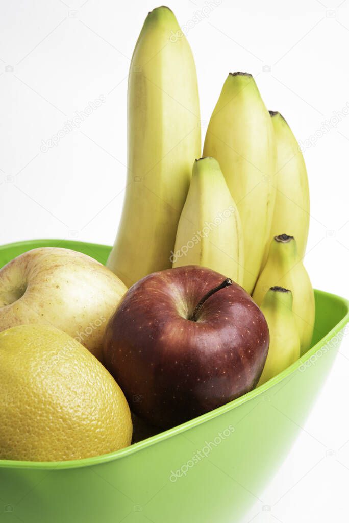 A bright green plastic bowl with artfully arranged fresh and ripe fruits such as apples, bananas, oranges, and others set on a plain white background.
