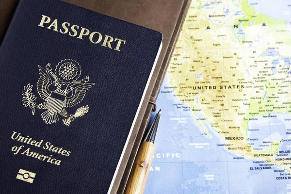 The foil-stamped dark blue front cover of an American passport with leather-covered travel notebooks and writing pen set on a world map background.