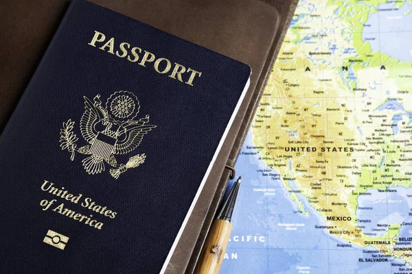 图上印着美国护照的箔印深蓝色封面 上面有皮革封皮的旅行笔记本 并在世界地图的背景上书写笔迹 — 图库照片