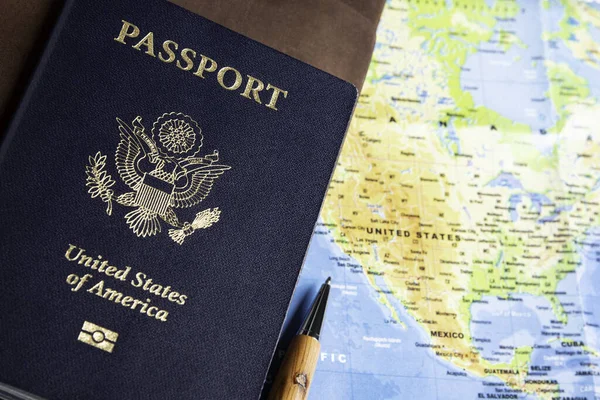 The foil-stamped dark blue front cover of an American passport with leather-covered travel notebooks and writing pen set on a world map background.