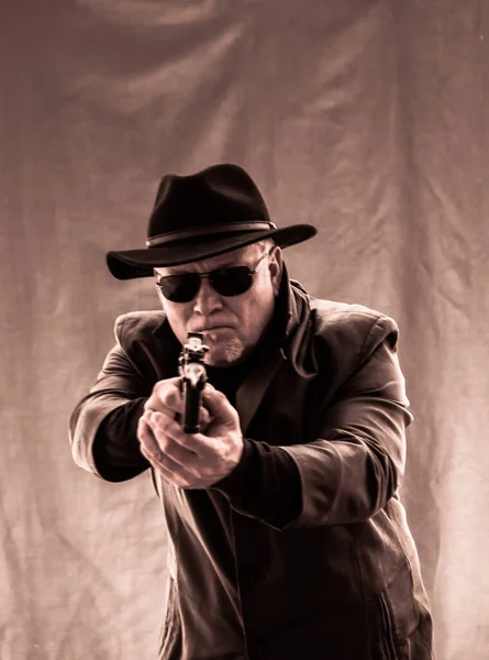 A man in black clothes, a black leather coat, hat. Ganster with a cigar and weapons, a Mauser system pistol. Mafiosi in black glasses on a dark background.  dangerous, unfriendly, evil, rude man. Cowboy felon