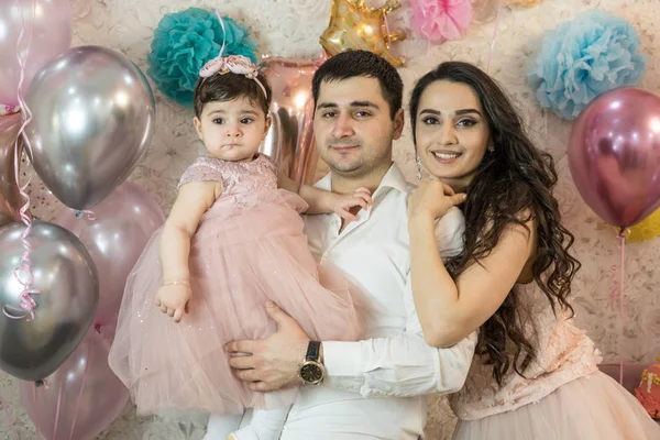 Bebeğin doğum günü kutlaması. Kız daha bir yaşındaydı. Mutlu ebeveynler. Çocuk başka yere bakıyor. Hepsi de şık giyinmiş. Genç, güzel evli bir çift ve Kafkas kökenli bir çocuk. Balonların arka planında, pembe renklerde..