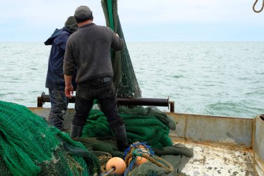 Balıkçılar iş başında. Denizciler balıkçı teknesini falcının güvertesine çeker. Ağın içinde balık yakaladım. Balık oltası. Karadeniz. Genel olarak bulutlu.