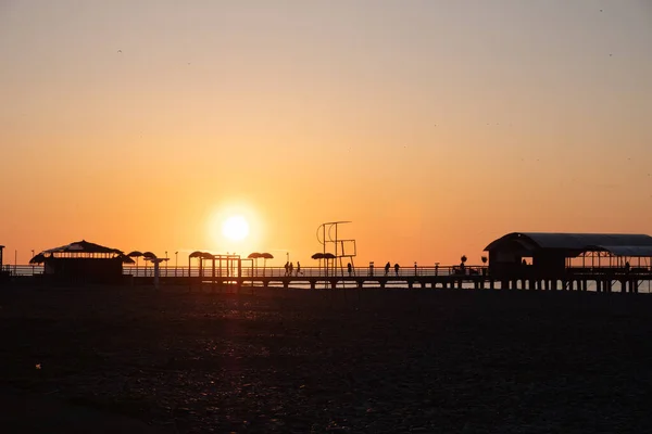 Sunset on the black sea. People walk along the beach and pier. Quiet, calm evening.