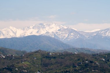 Kafkasya 'nın eteklerinin manzarası. Batumi ilçesi. Yüksek tepelerde kar yatıyor. Alt dağlarda yerleşim yerleri var. Arazinin rengi farklı..