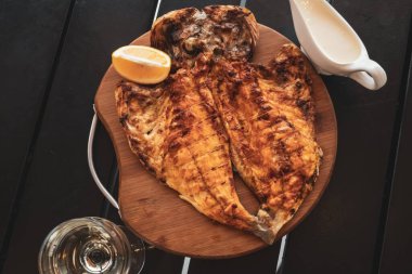 Golden Spar, Dorado ya da ızgarada pişmiş Aurata. Tahta tabakta altın renkli balık. Limon, sos kabında sarımsak sosu. Bir bardak beyaz şarap. Deniz ürünleri restoranı. Günaydın Georgia..